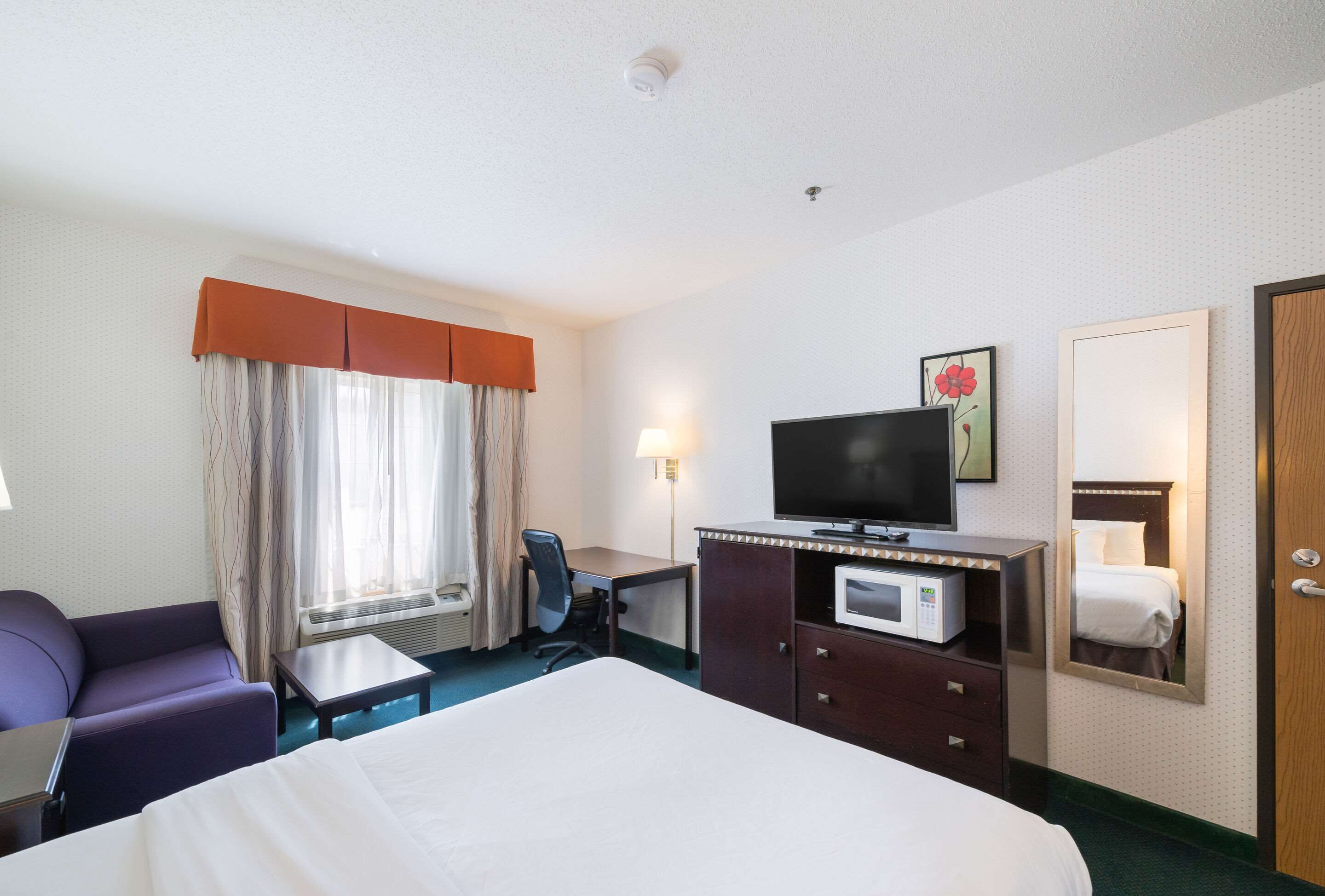 A hotel room with a bed, a desk, a chair, a television, a microwave, and a mirror.