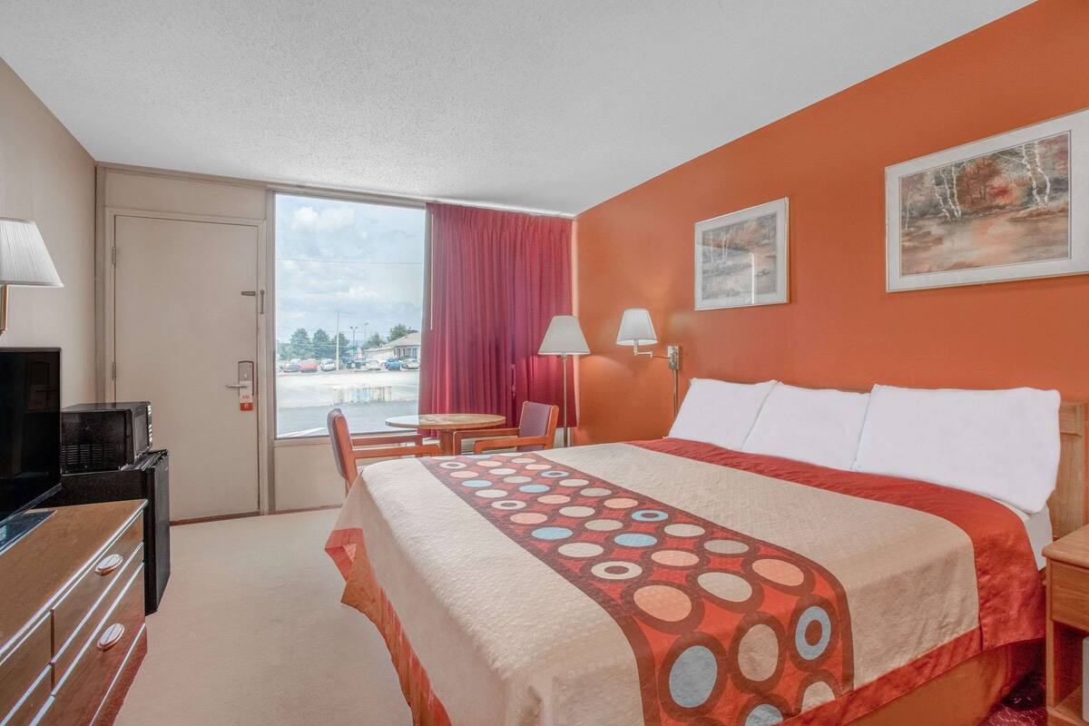 A hotel room with a bed, a desk with a computer, a chair, a window with a view of the outside, and a door.