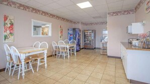 A dining area with a white table and chairs, a vending machine, and a refrigerator.