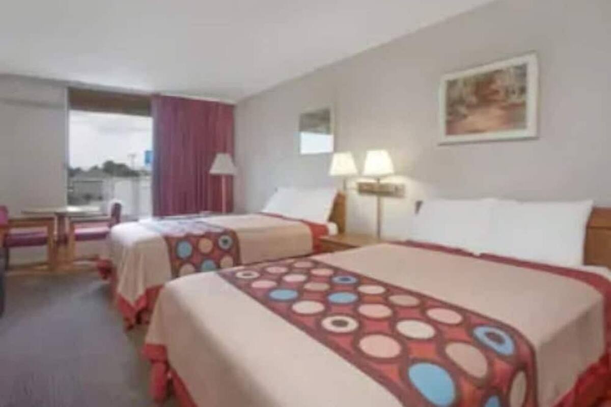 A hotel room with two beds, a desk, and a window.