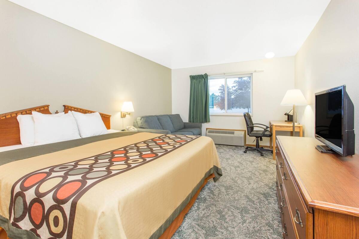 A hotel room with a bed, a desk, a chair, a television, and a window with curtains.