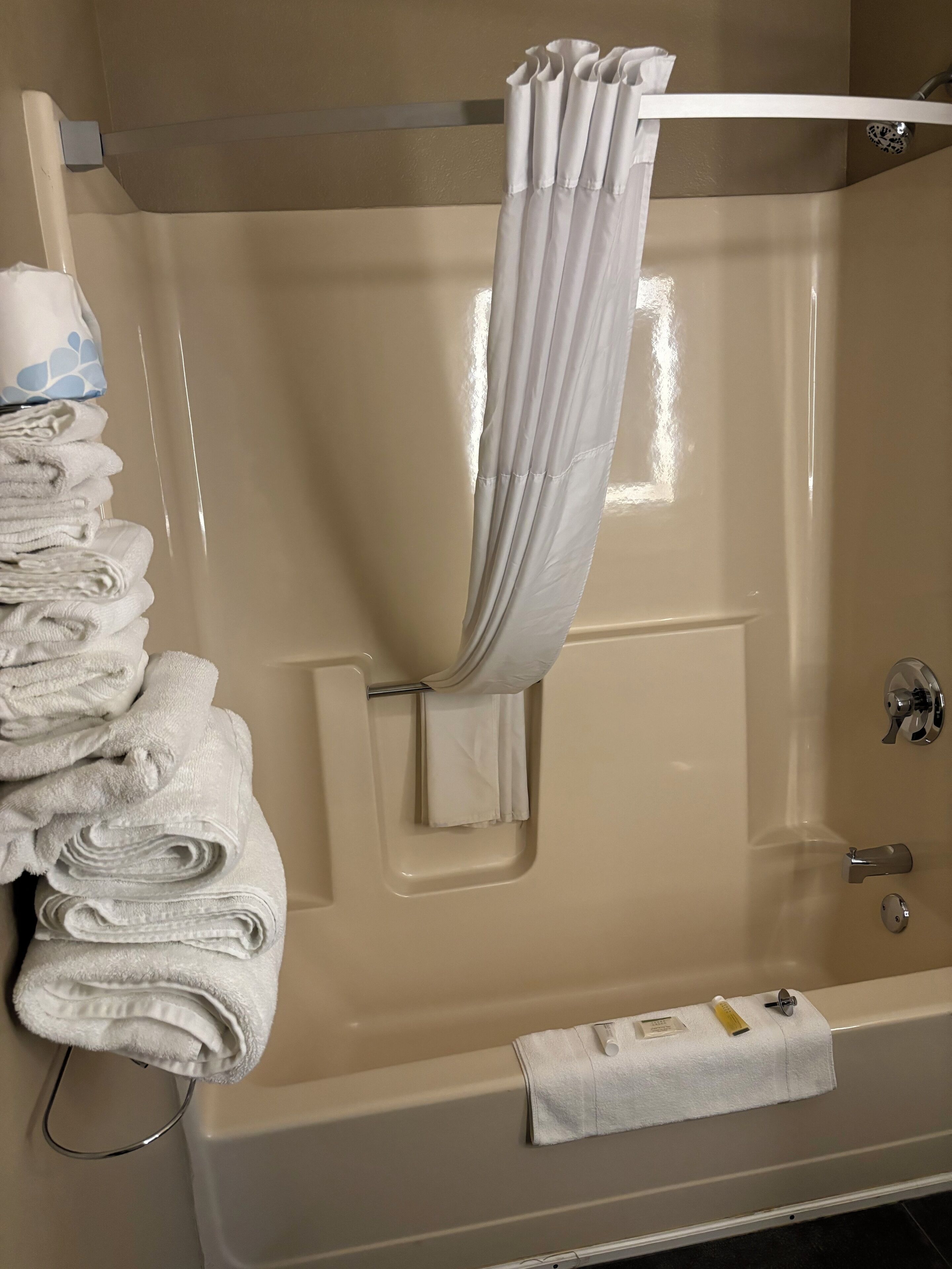 A bathroom with a bathtub, a towel rack with folded towels, a shower curtain, and a visible door handle.