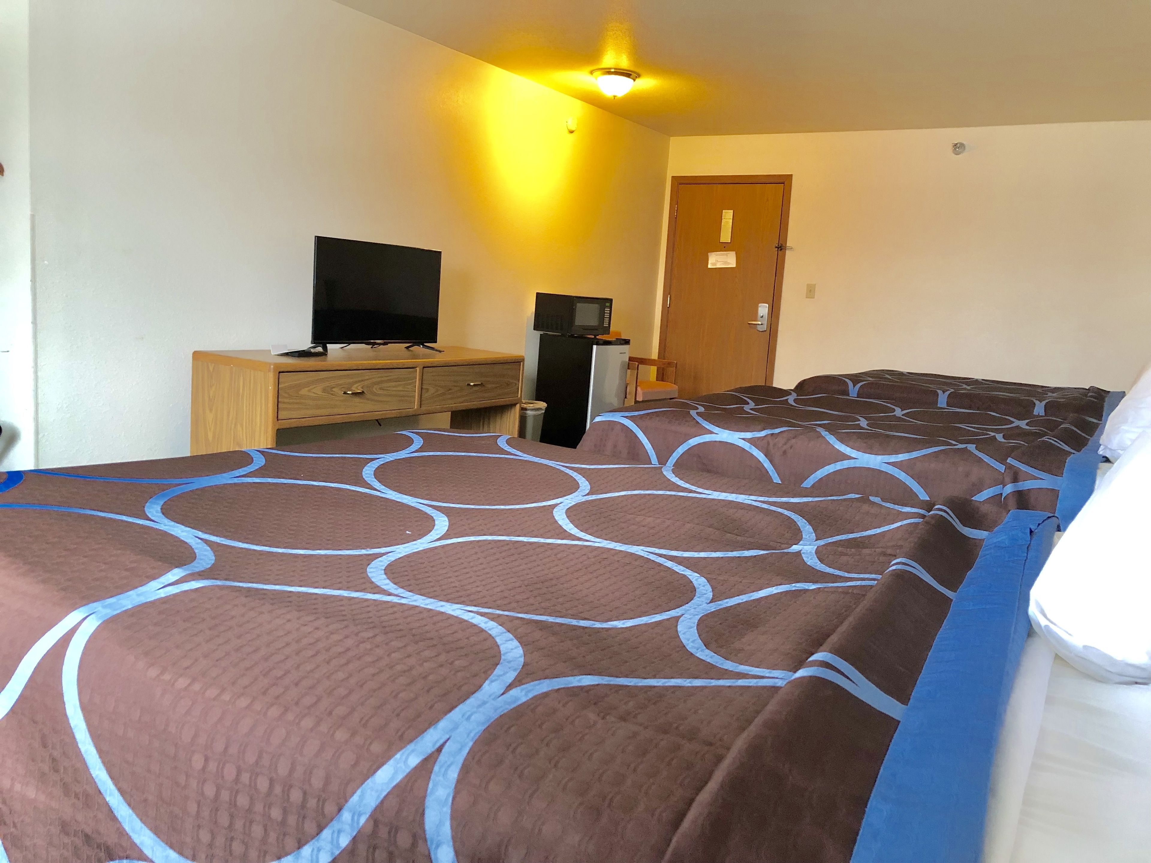 A hotel room with a large bed, a television, a refrigerator, and a wooden dresser.