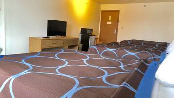 A hotel room with a large bed, a television, a refrigerator, and a wooden dresser.