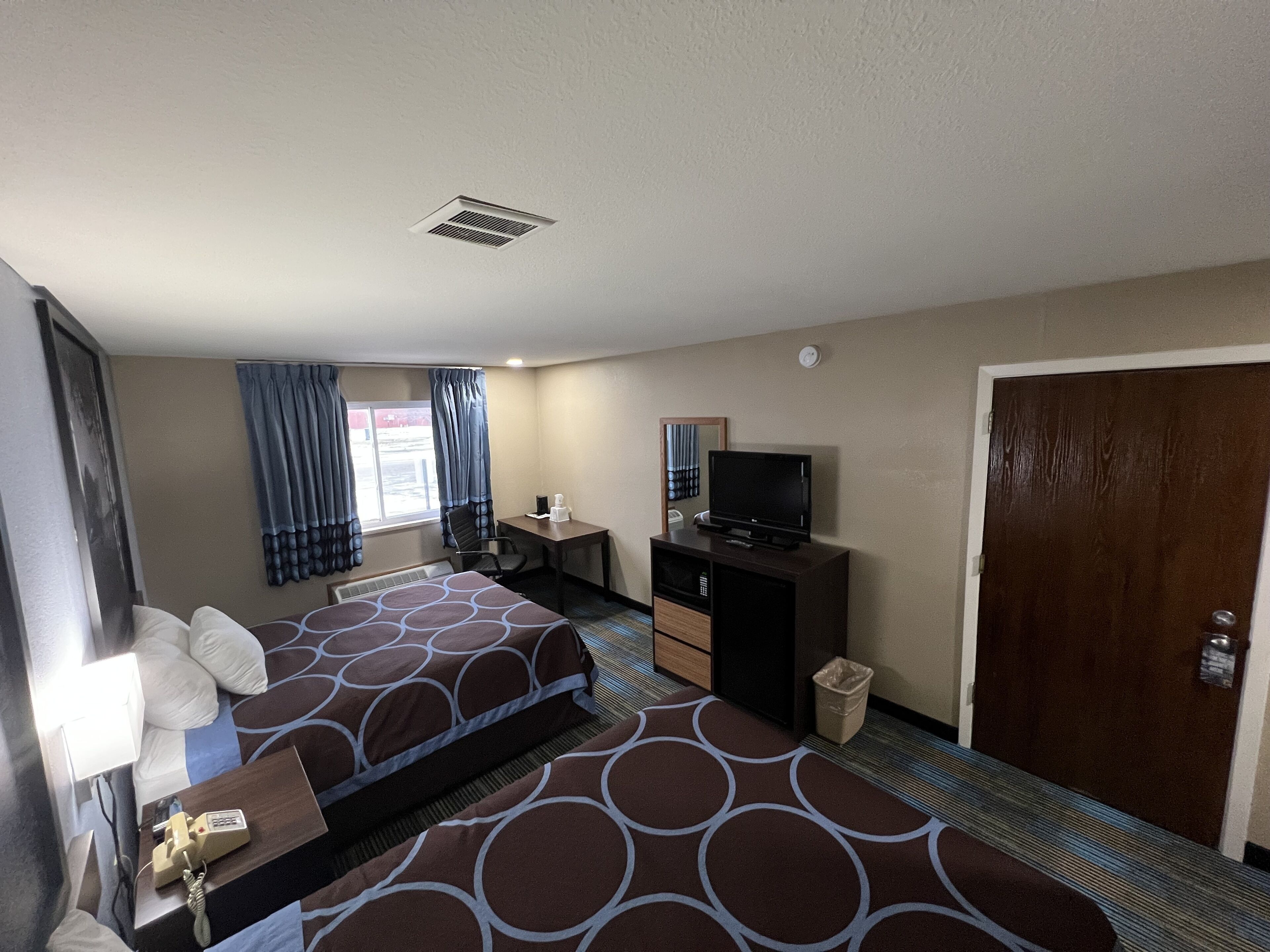 A hotel room with two beds, a desk, a television, and a door.
