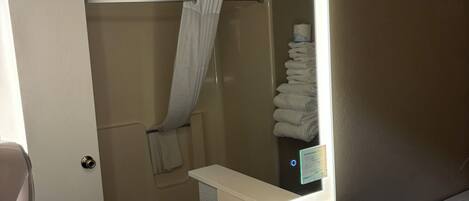 A bathroom with a large mirror, a sink, a shower, and a towel rack.