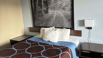 Quarto de hotel com uma cama grande, cabeceira com arte de tema florestal, mesa de cabeceira com abajur e um tapete listrado.