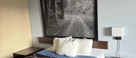 A hotel room with a large bed, a headboard with a forest-themed artwork, a bedside table with a lamp, and a striped carpet.