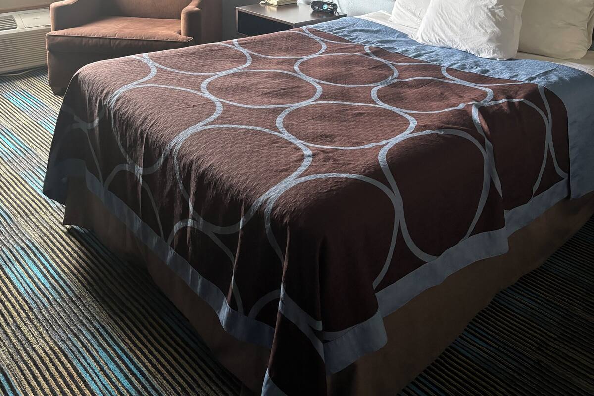 A hotel room with a large bed, a chair, a nightstand with a lamp, and a painting on the wall.