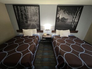 A hotel room with two beds, a nightstand, a lamp, and two framed pictures on the wall. - Super 8 by Wyndham Escanaba (Escanaba)