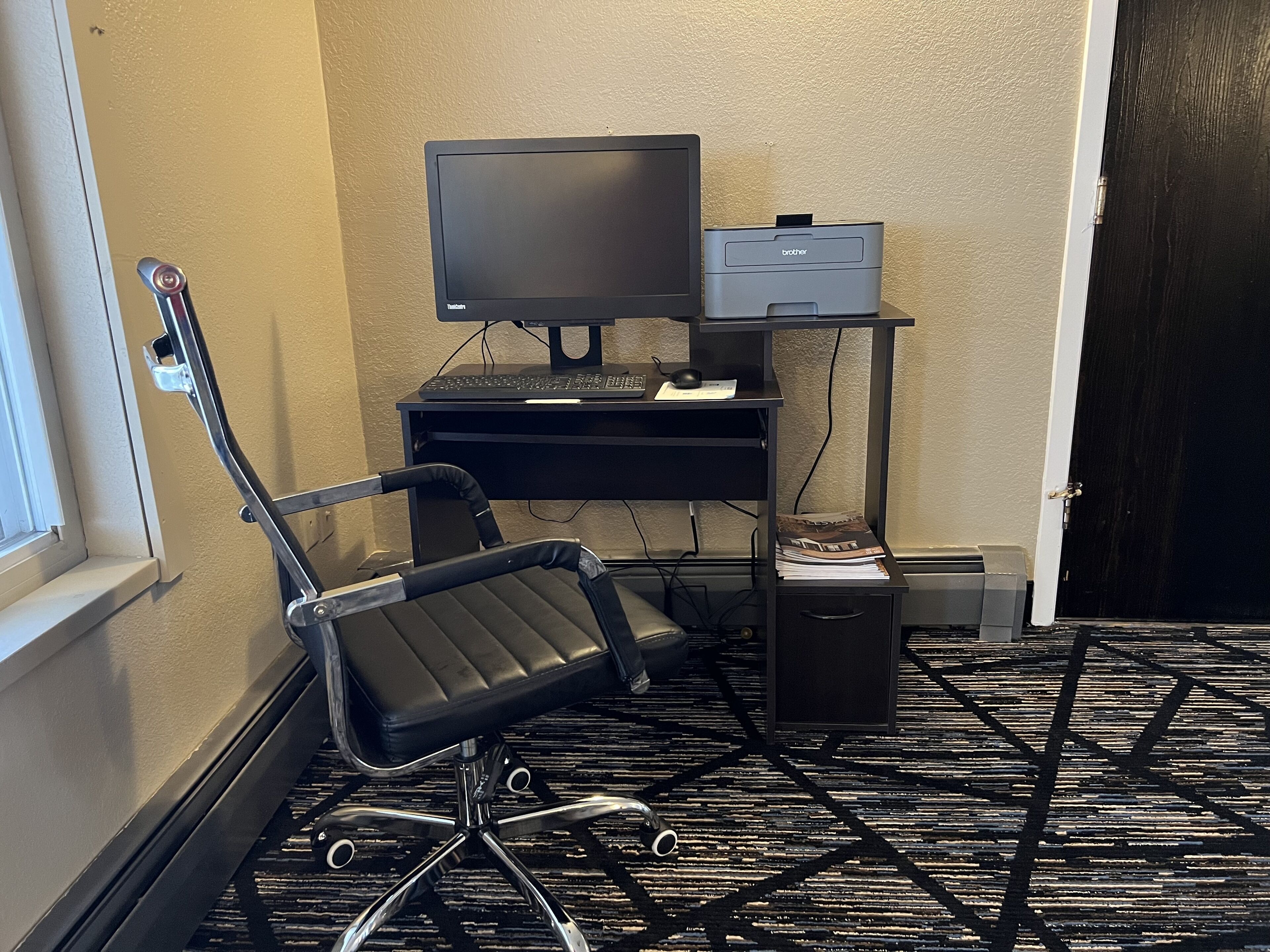 A corner office with a desk, chair, computer, and printer.