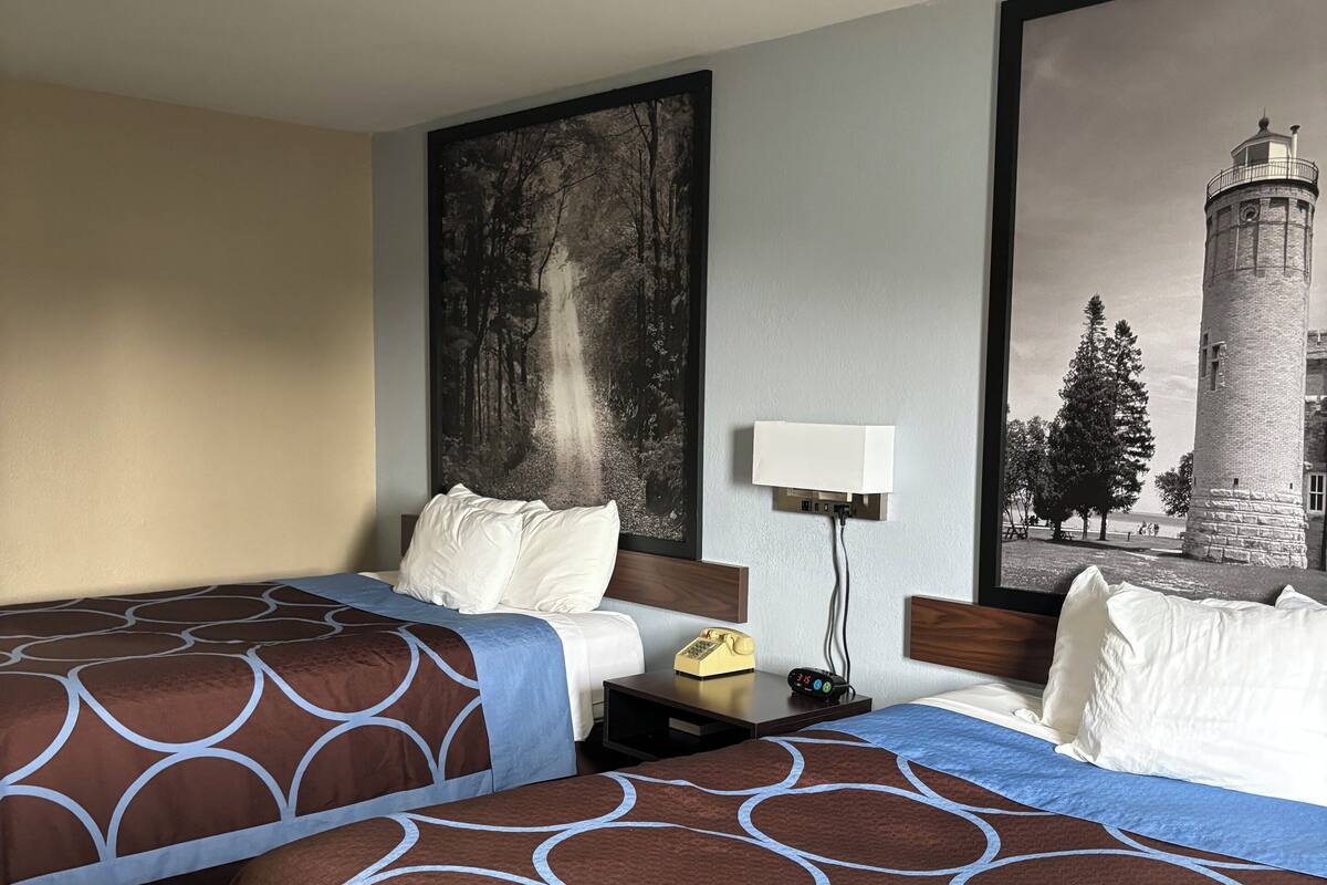 A hotel room with two beds, a nightstand, a lamp, and a large framed picture of a lighthouse.