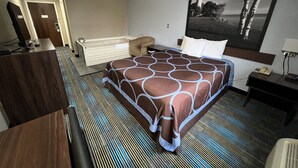 Habitación de hotel con una cama grande, un escritorio, una silla, una lámpara de escritorio, un teléfono y un cuadro de un faro.