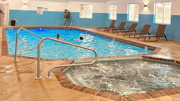 Una piscina interior con hidromasaje, sillones de descanso y techo de madera.