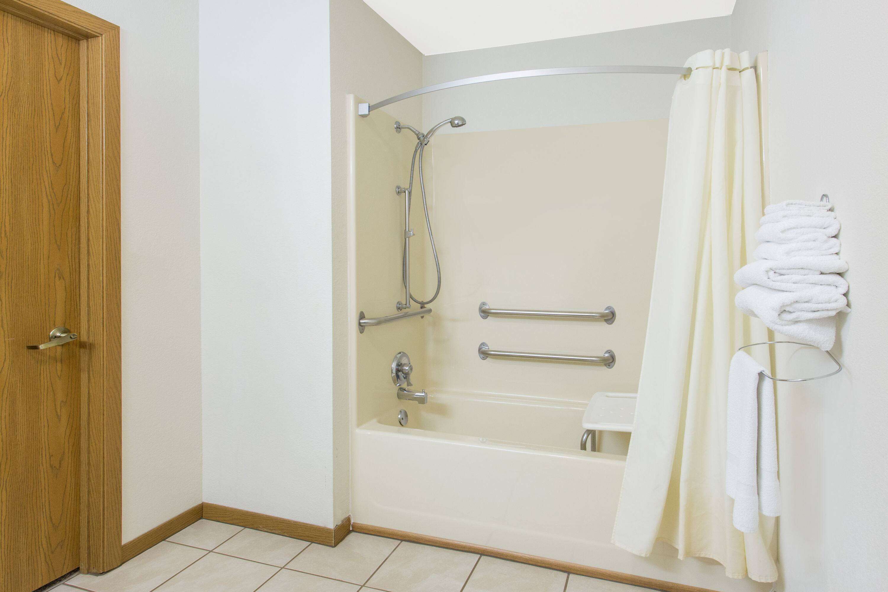 A bathroom with a shower, grab bars, and a towel rack.