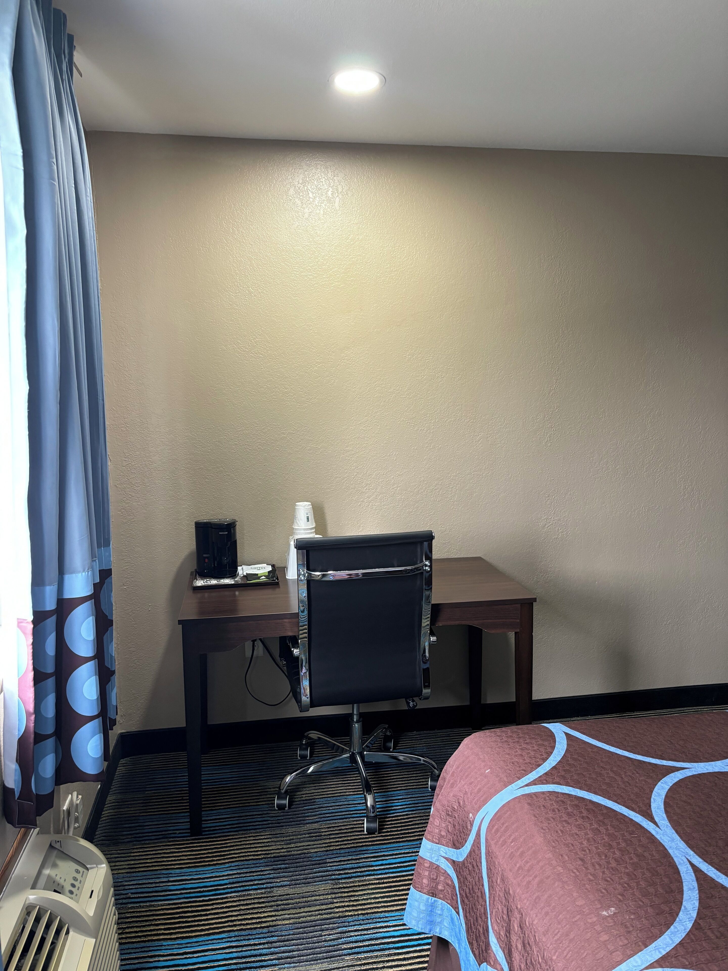 Habitación de hotel con cama, escritorio, silla, cafetera y calefacción.