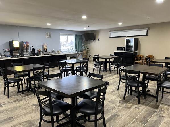 Un restaurante con varias mesas y sillas, una barra con dispensador de bebidas y un televisor montado en la pared.