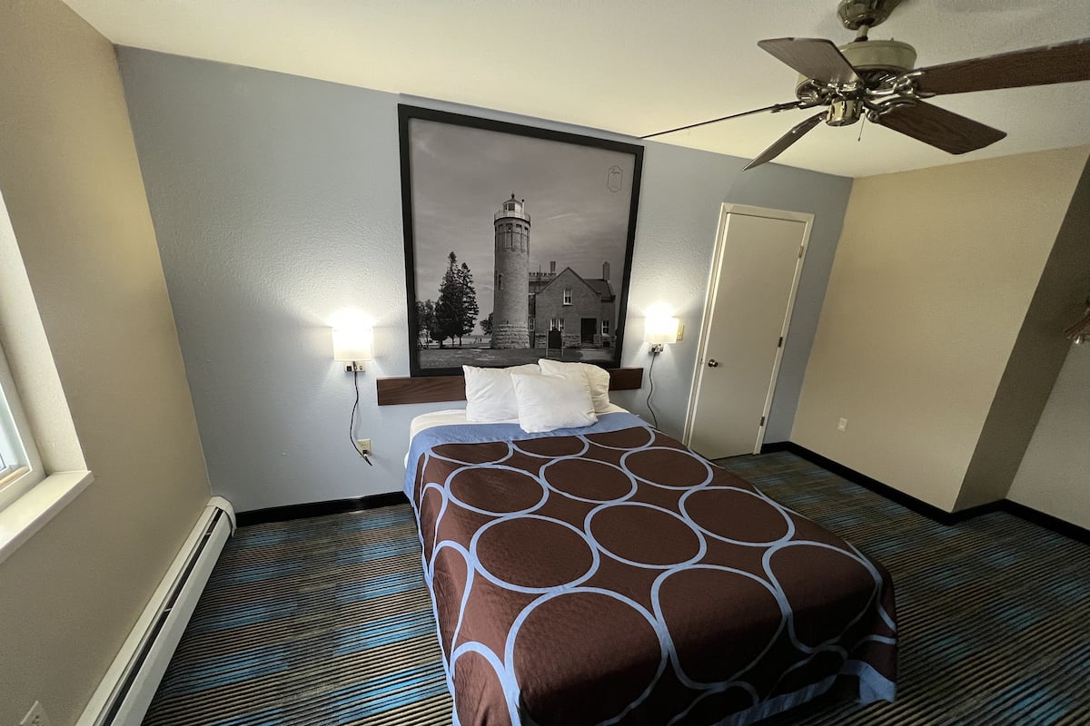 A hotel room with a bed, a ceiling fan, a framed picture on the wall, and a door.