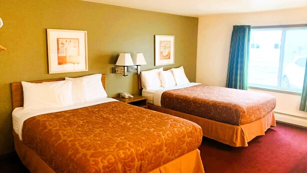 Habitación de hotel con dos camas, una mesita de noche con lámpara y cuadros en la pared.