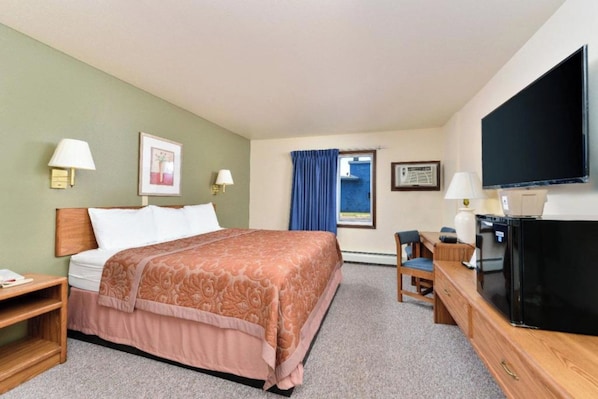 Una habitación de hotel con cama, escritorio, silla, televisión y ventana con cortinas.