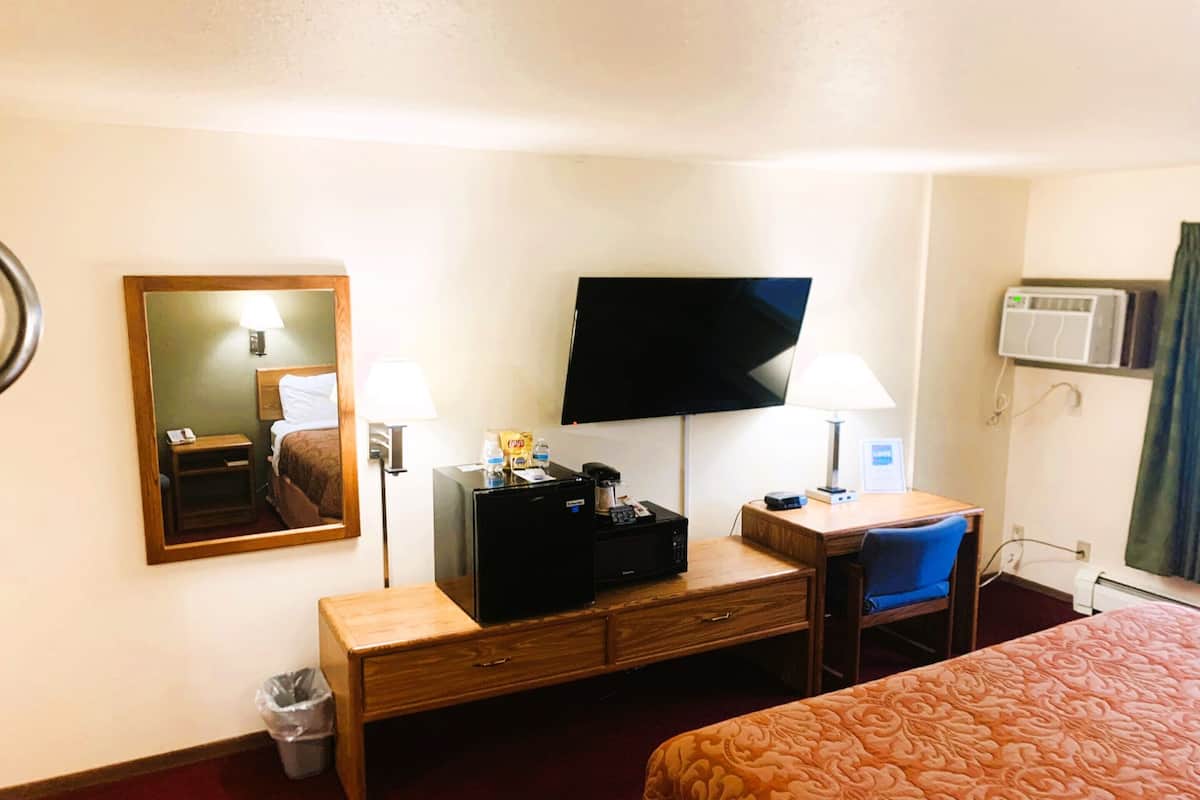 A hotel room with a bed, a desk with a computer, a chair, a TV, and a trash can.