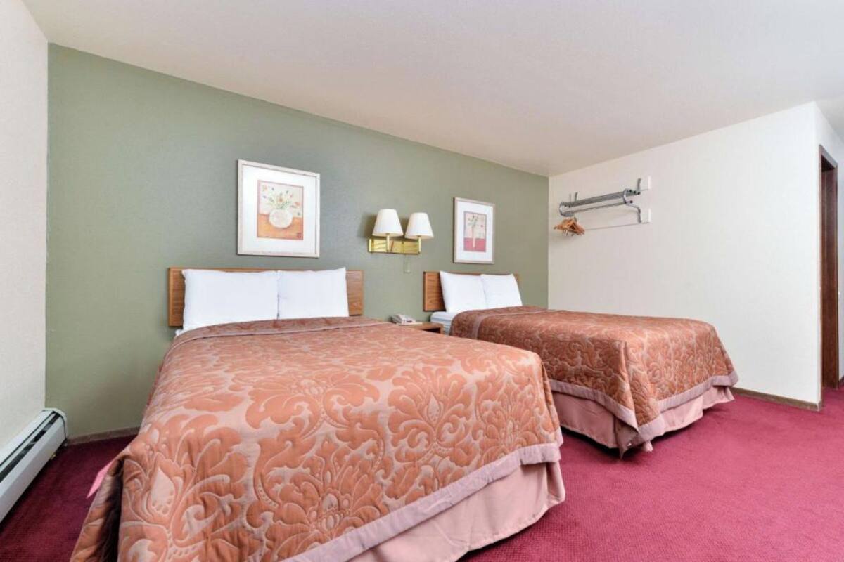 A hotel room with two beds, a red carpet, and framed artwork on the walls.
