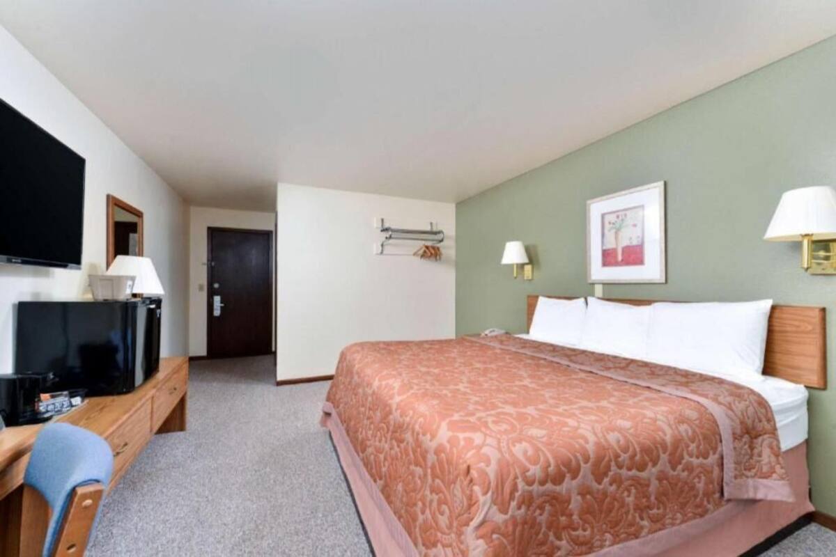 A hotel room with a bed, a television, a desk, and a door.
