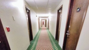 Un pasillo de hotel con alfombra estampada, puertas a ambos lados y un detector de incendios en la pared izquierda.