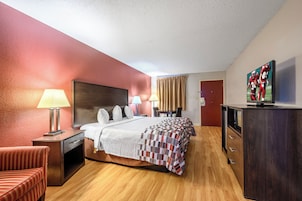 Una habitación de hotel con una cama, lámparas de noche, televisor, escritorio y una silla.