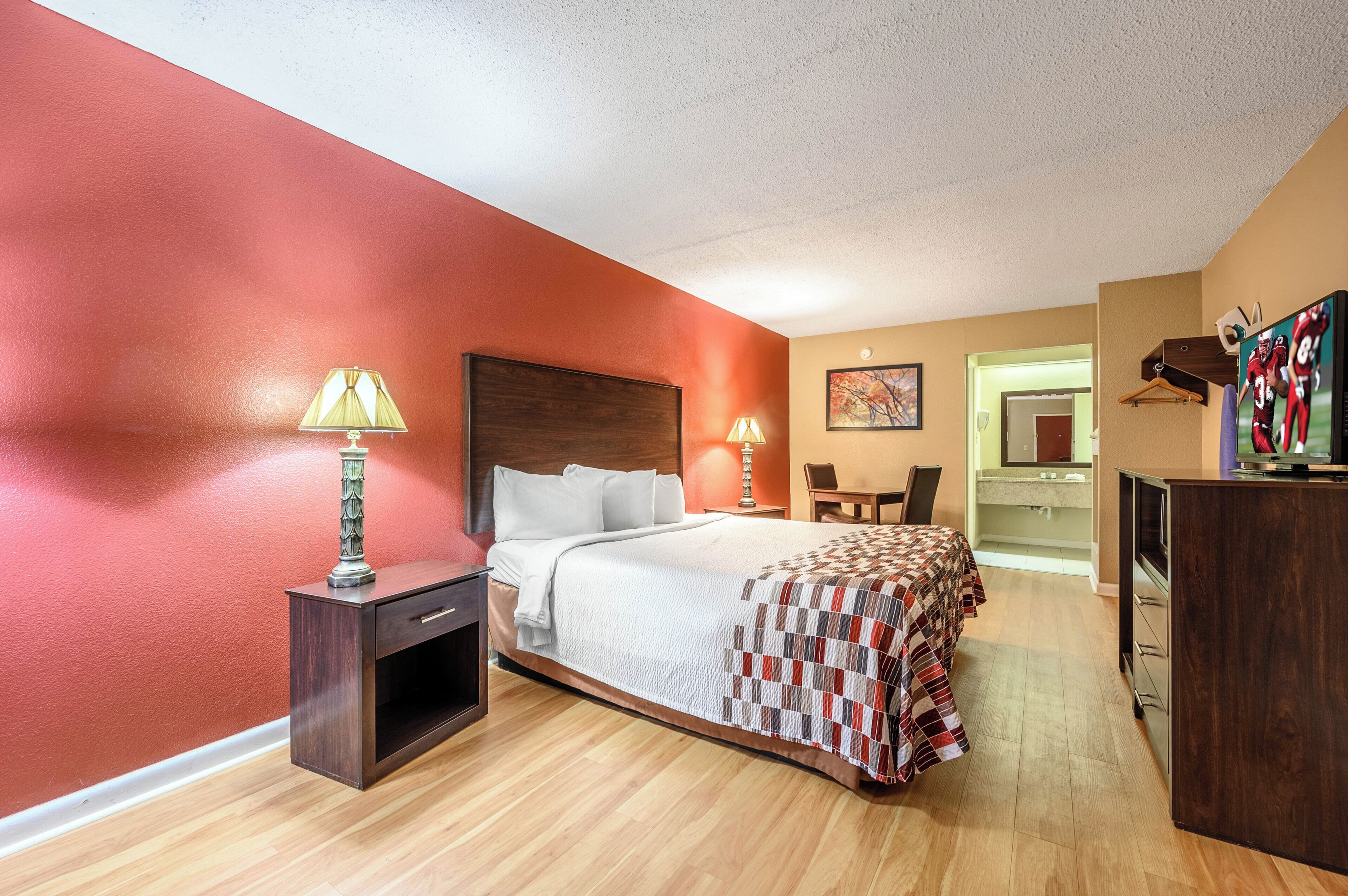 A hotel room with a bed, bedside lamps, a desk, a chair, and a television.
