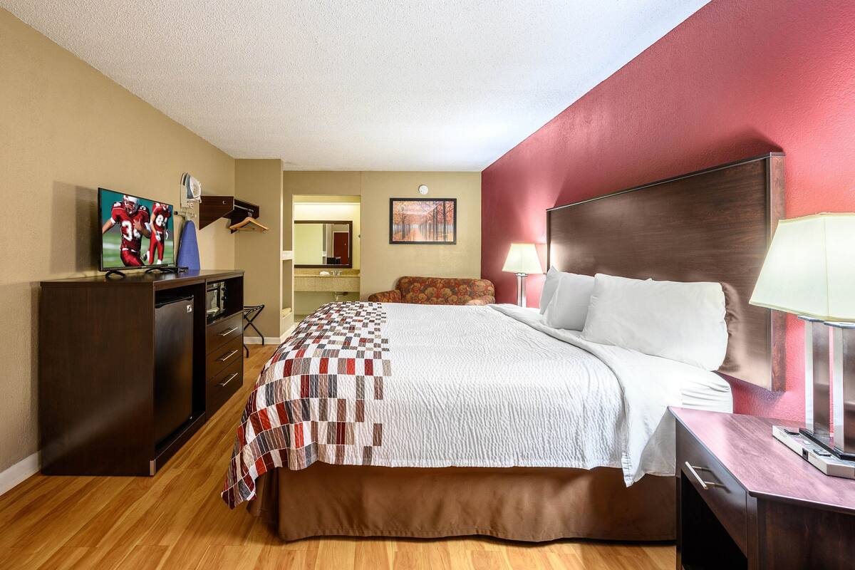 A hotel room with a bed, a desk, a TV, and a mirror.