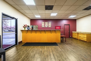 Una zona de recepción con un mostrador de madera, una puerta roja y un ventanal con vista a un estacionamiento.