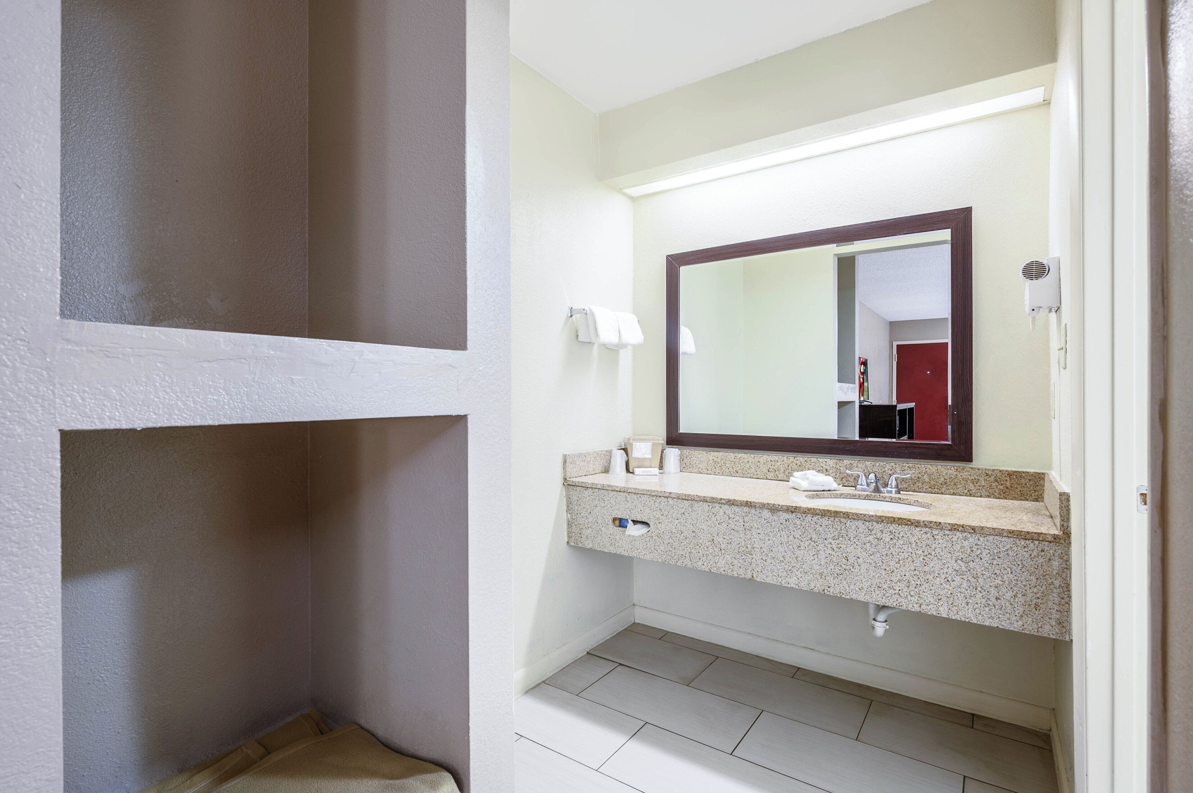 Un baño con encimera de granito, lavamanos, espejo y toallero.