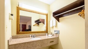 A bathroom with a granite countertop, a gold-framed mirror, a towel rack, and a wooden shelf. - Red Roof Inn Sylacauga (Sylacauga)
