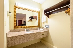 A bathroom with a granite countertop, a gold-framed mirror, a towel rack, and a wooden shelf. - Red Roof Inn Sylacauga (Sylacauga)