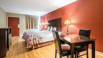 Una habitación de hotel con cama, escritorio, silla, lámpara y puerta.