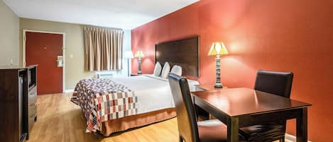 Une chambre d’hôtel avec un lit, un bureau avec une chaise, une lampe et une porte.