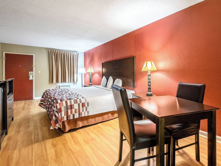 A hotel room with a bed, a desk with a chair, a lamp, and a door.