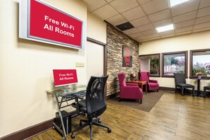 A hotel room with a desk, chairs, a stone accent wall, and a sign indicating free Wi-Fi in all rooms. - Red Roof Inn Sylacauga (Sylacauga)