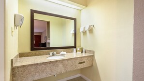 A bathroom with a granite countertop, a sink, a mirror, and a towel rack. - Red Roof Inn Sylacauga (Sylacauga)