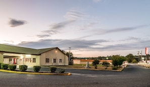 A building with a green roof and a Coca-Cola sign, a parking lot, and a clear sky. - Red Roof Inn Sylacauga (Sylacauga)