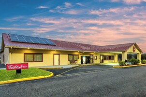 A Red Roof Inn with a solar panel roof, a parking lot, and a clear sky.