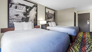 A hotel room with a large bed, a smaller bed, a nightstand with a lamp, and two large framed pictures on the wall. - Super 8 by Wyndham Farmington (Farmington)