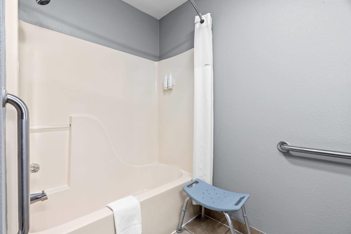 Une salle de bain équipée d’une baignoire, d’un rideau de douche, d’une barre d’appui et d’un petit marchepied.