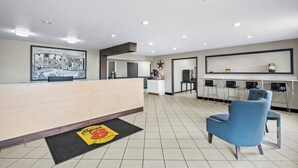 A hotel lobby with a reception desk, a blue armchair, a wall-mounted clock, and a framed welcome sign. - Super 8 by Wyndham Farmington (Farmington)