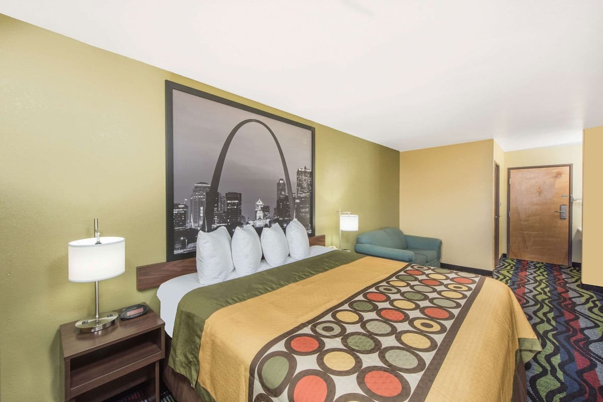 Une chambre d’hôtel avec un lit, un tableau représentant un paysage urbain, un bureau avec une lampe et une moquette à motifs.
