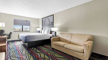 Habitación de hotel con cama, sofá, escritorio y una ventana grande con vista a la ciudad.