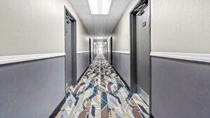 A long, narrow hallway with patterned carpet, doors on both sides, and a ceiling light. - Super 8 by Wyndham Farmington (Farmington)
