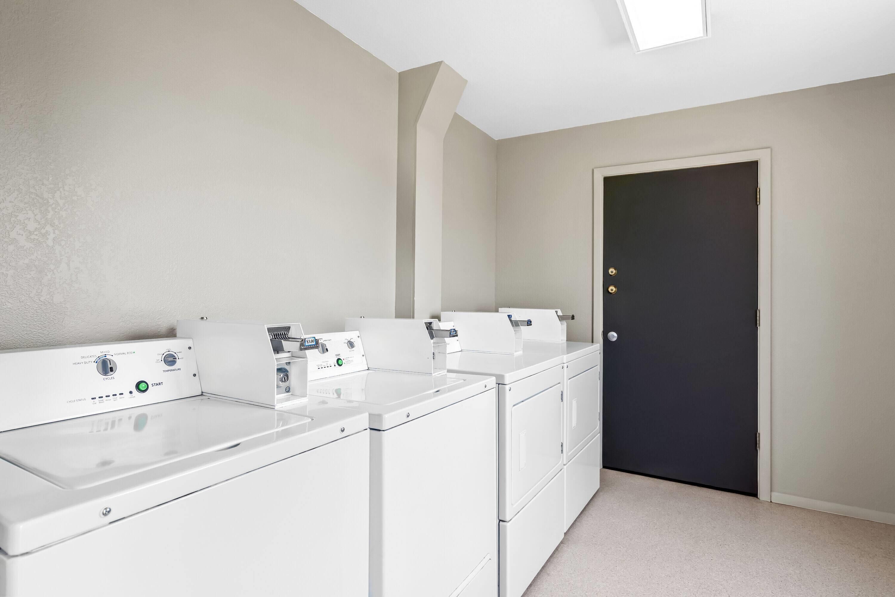 A laundry room with four white washers and dryers, a door, and a light fixture.