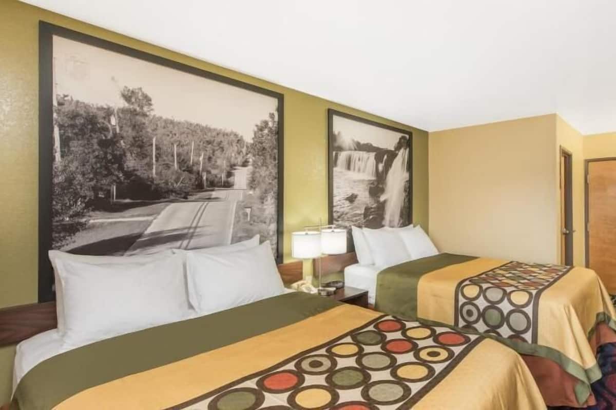 Une chambre d’hôtel avec deux lits, une table de chevet, une lampe et deux grandes images encadrées au mur.
